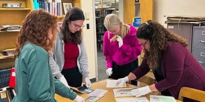 Three college students and one library director wearing latex gloves stand around a table and work with documents and artifacts