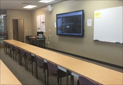 Empty classroom with desks and chairs facing a digital screen