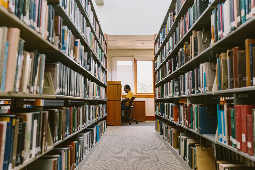 AMBS student Workineh Yami sitting at a desk in the library with bookshelves on the left and right