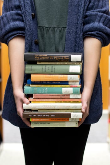 Photo of a person from the shoulders down standing and holding a stack of books