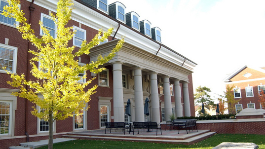DePauw University building with pillars and benches on a patio next to a leafy tree.