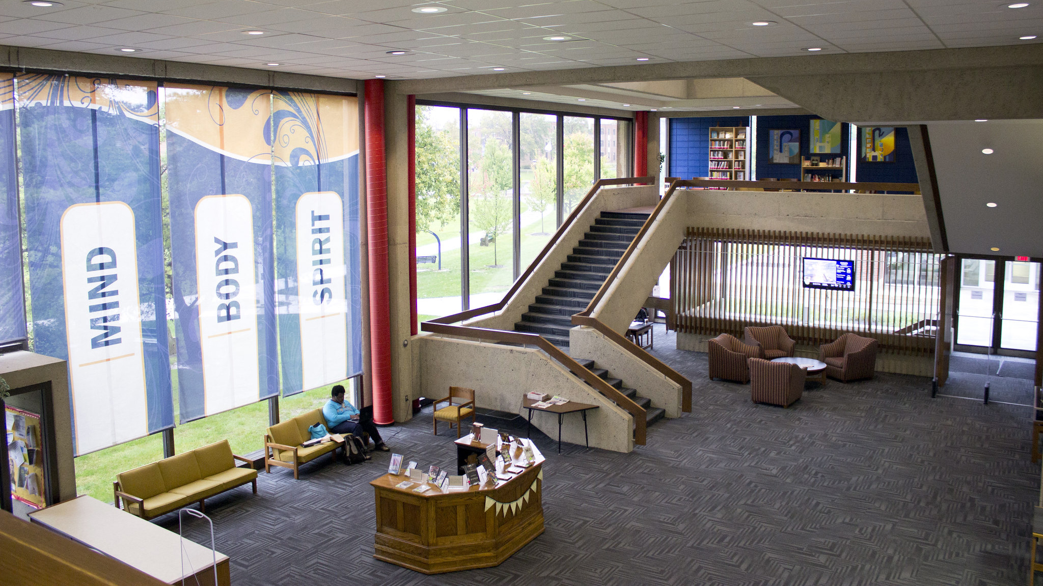 Inside Marian University Library with staircase and help desk in front of floor-to-ceiling windows
