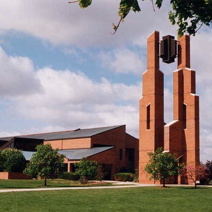 Outdoor shot of Taylor University's Zondervan Library, a brick building with a tiered tower among green grass and trees.